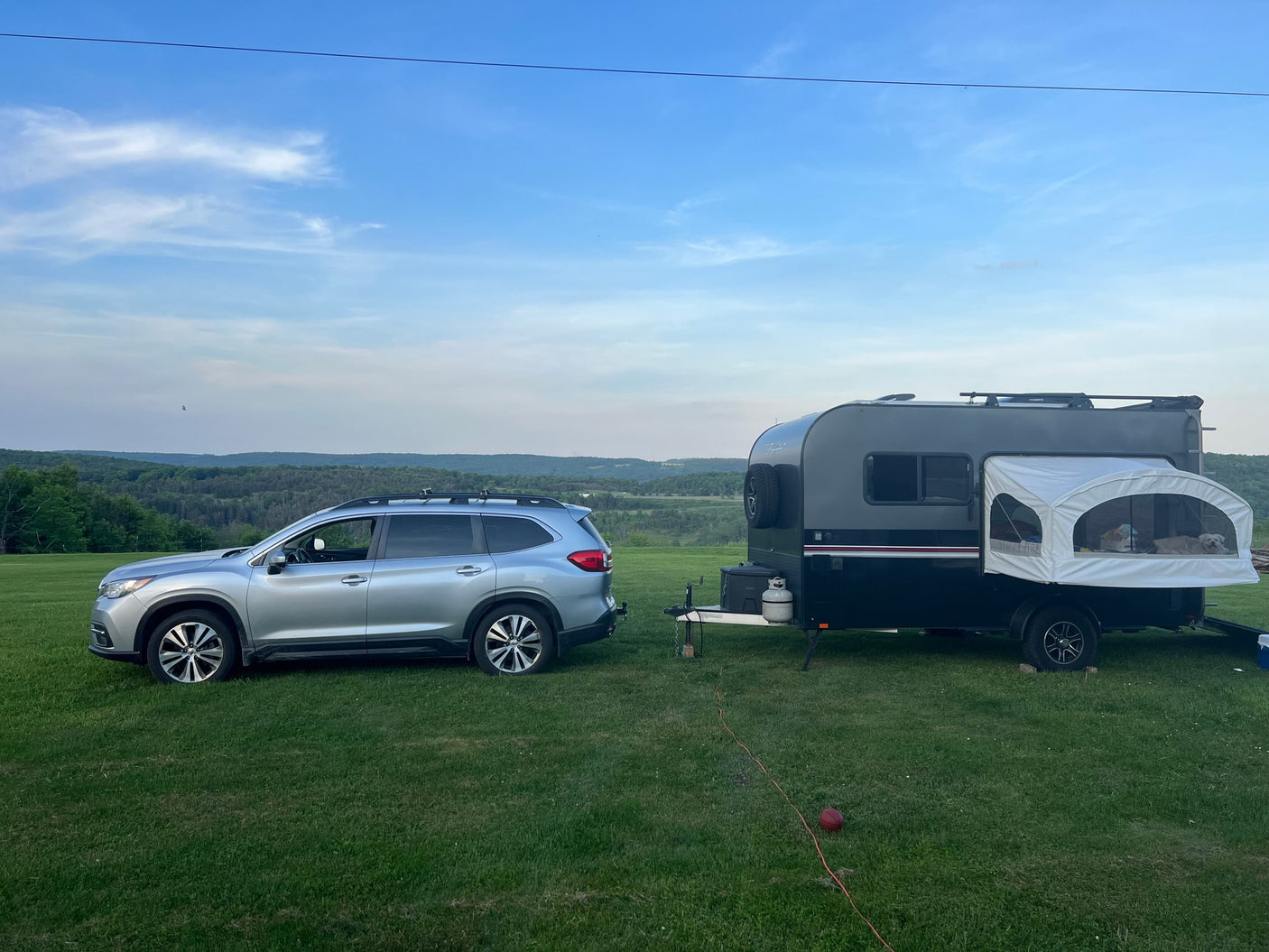 RV rental: A silver SUV tows a dark camper, dogs visible in the pop-out bed, set against a scenic valley view.