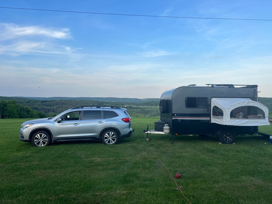 RV rental: A silver SUV tows a dark camper, dogs visible in the pop-out bed, set against a scenic valley view.