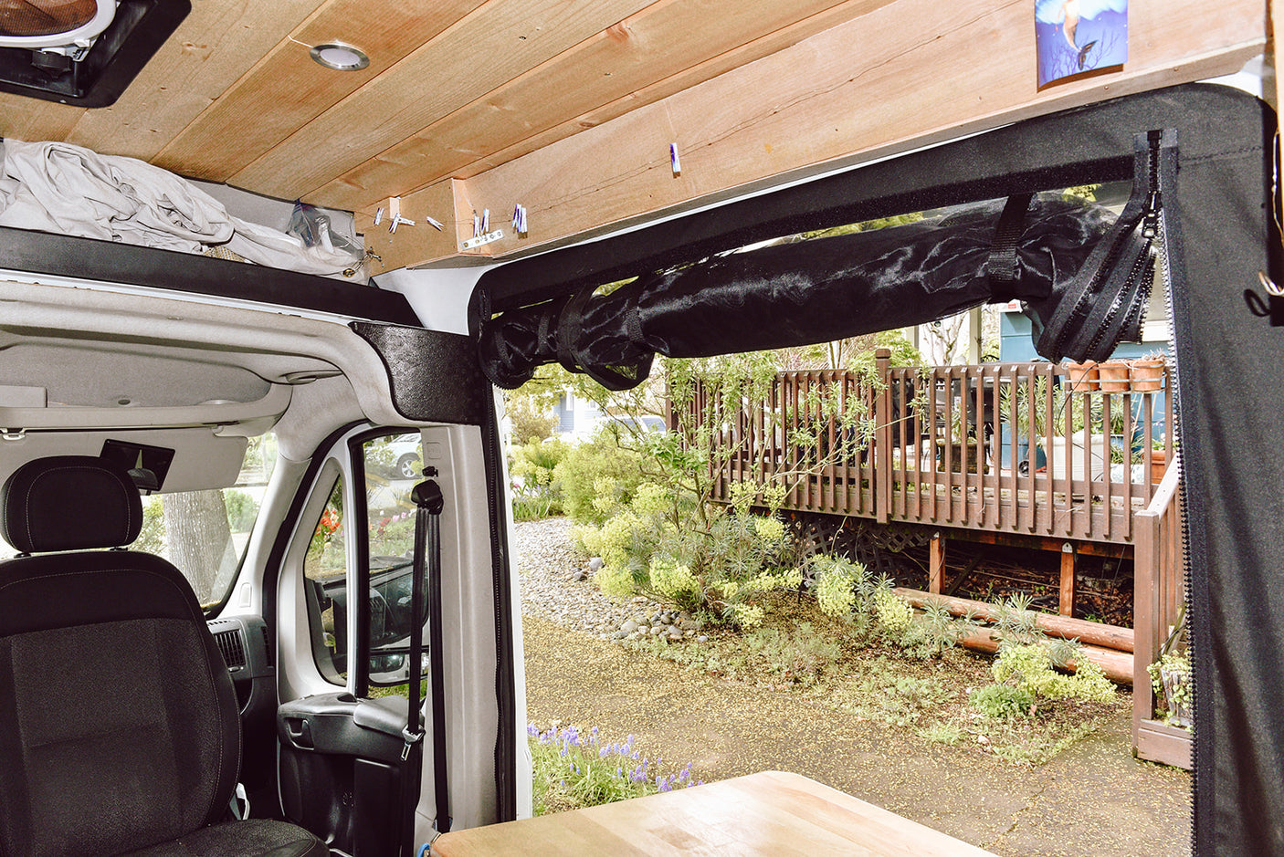 RV rental interior with wooden ceiling, rolled black screen, and garden view from the open side door.