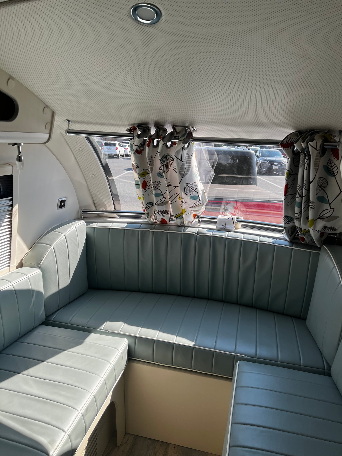 Relaxing RV rental interior with light blue cushioned seating, artistic curtains, and sunny window view.