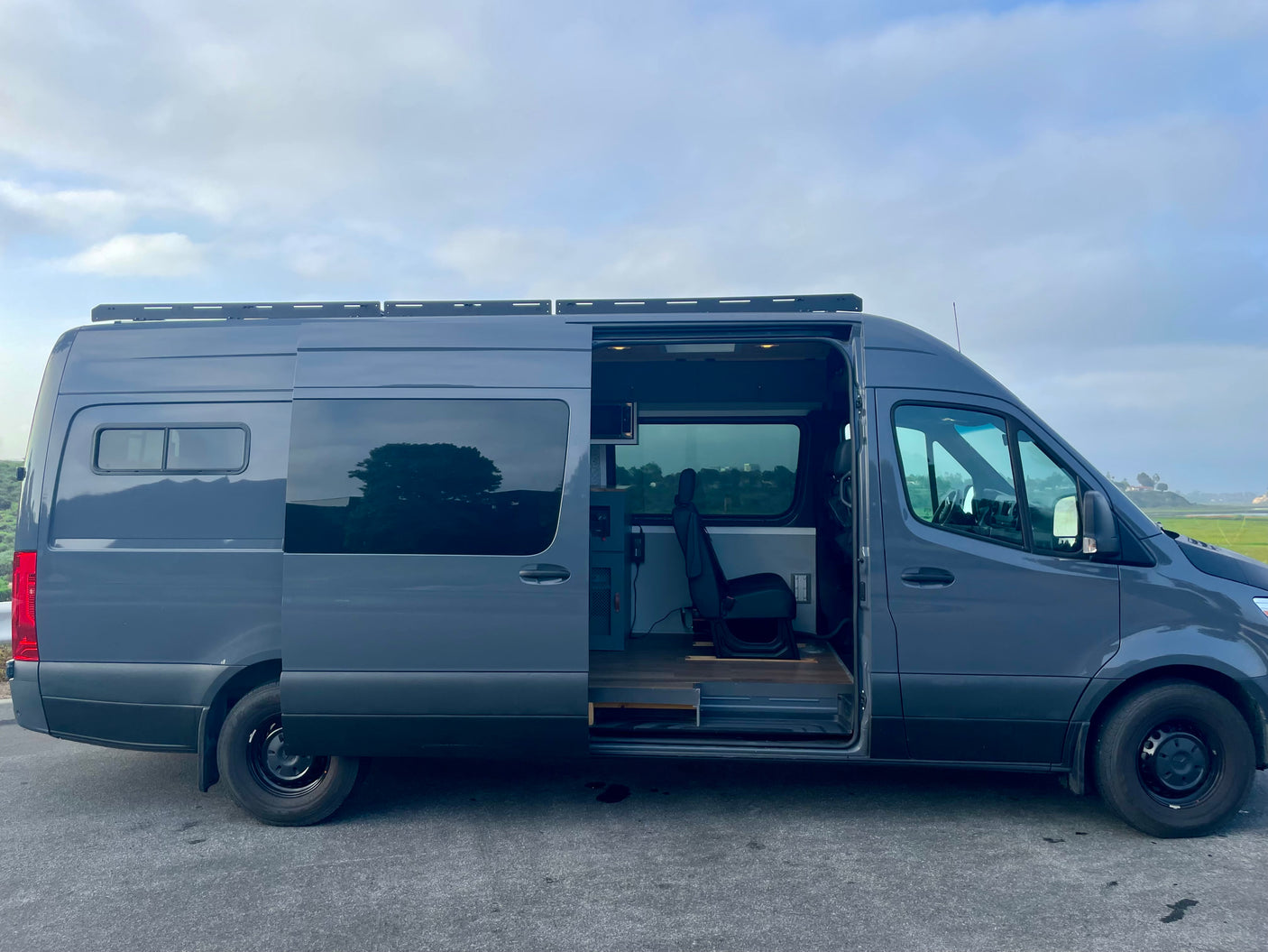 Gray Mercedes Sprinter camper van, great for RV rental, with side door open revealing custom interior. Ready for your travels.