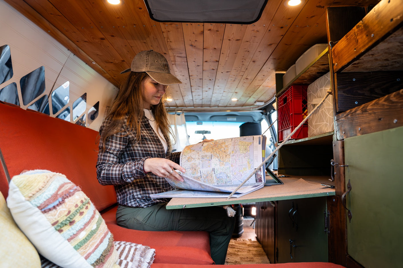 A woman plans her trip in a cozy RV rental, studying a large map book inside the wood-paneled van.