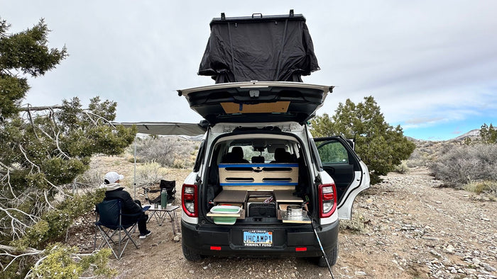 with a rooftop tent & awning set up for camping in mountains.|White SUV RV rental setup for car camping