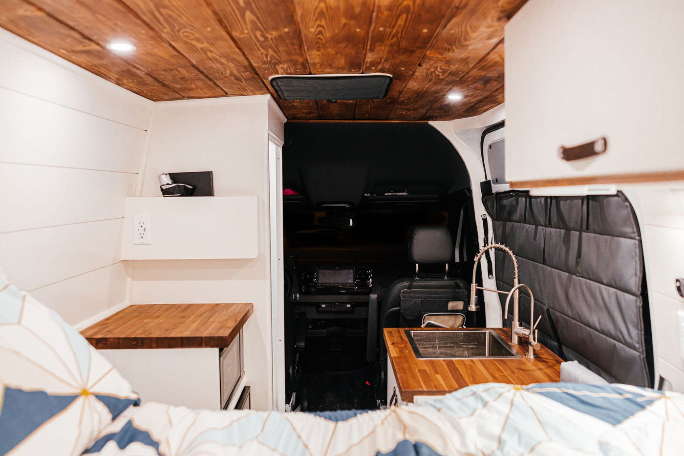 showing efficient van living.|Wake up to majestic red rock landscapes from your RV rental bed. Experience van life adventure and stunning nature views!|White camper van RV rental with rooftop solar panels & AC unit on asphalt.|Compact shower with handheld head and mirror — photo 8