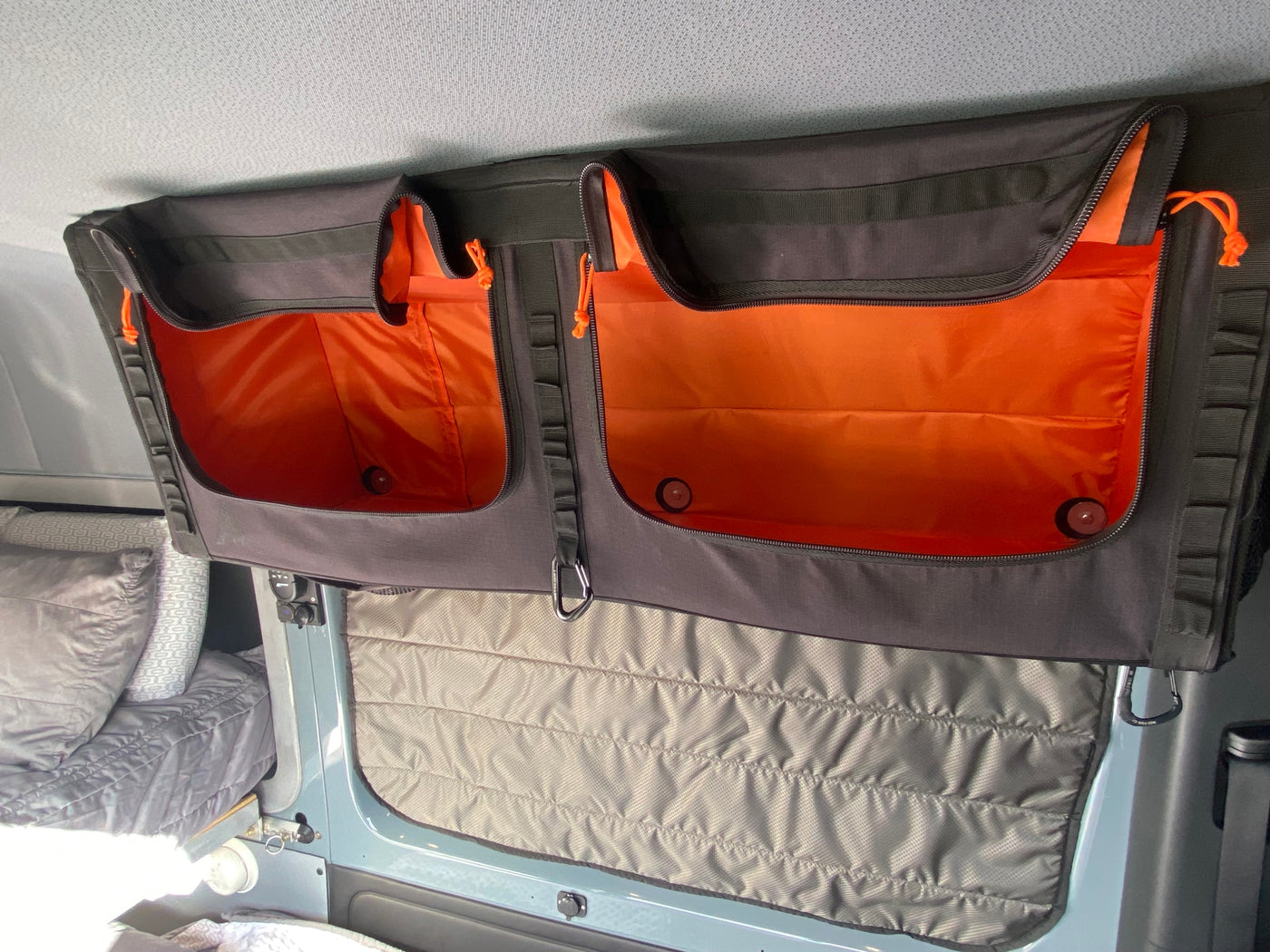 RV rental overhead storage pockets with bright orange interiors and quilted window insulation visible inside a camper. — photo 17