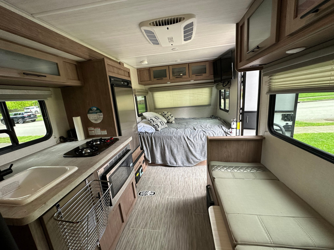 This RV rental features a full kitchen with sink/stove, a cozy bed, and dinette seating with outdoor views.