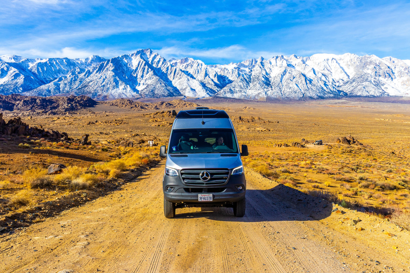 An RV rental camper van parked on a dirt road, with majestic snow-capped mountains and a desert landscape in the background.
