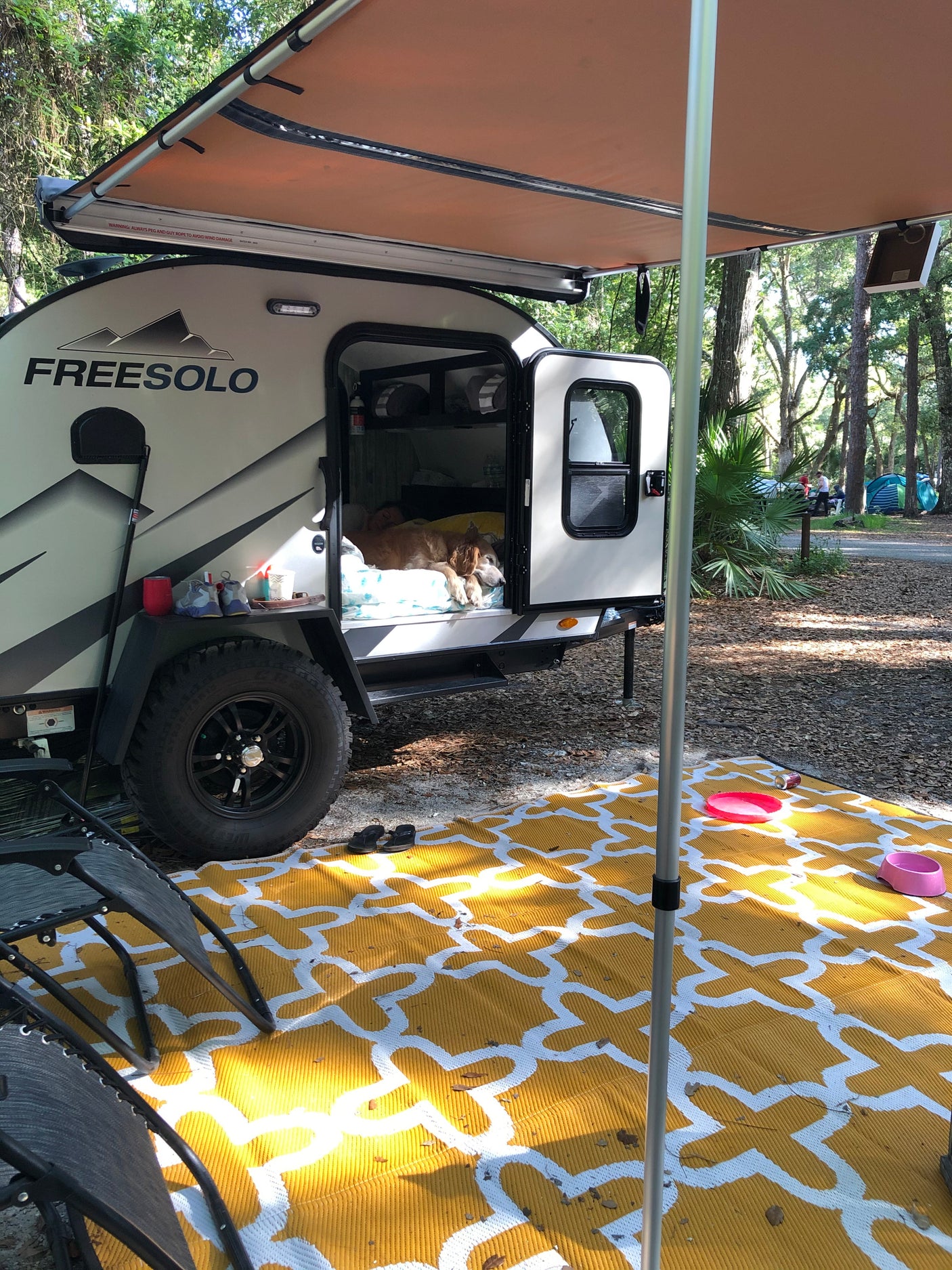 Relaxing at a campsite with an RV rental. A dog naps in the FREESOLO travel trailer, shaded by its awning.