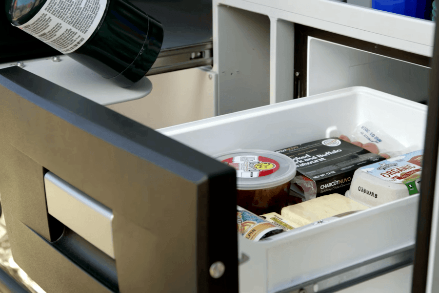 An RV rental's pull-out fridge, part of an outdoor kitchen, holds food like brats & organic eggs for camping meals.