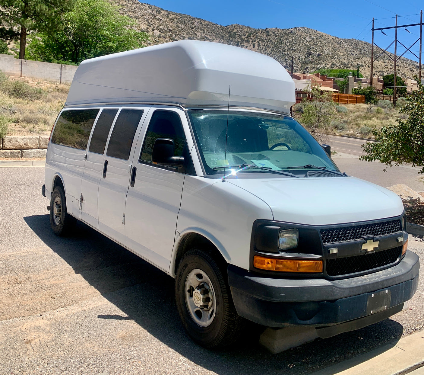 White high-top Chevrolet Express van for rv rental, parked outdoors against a mountain backdrop.