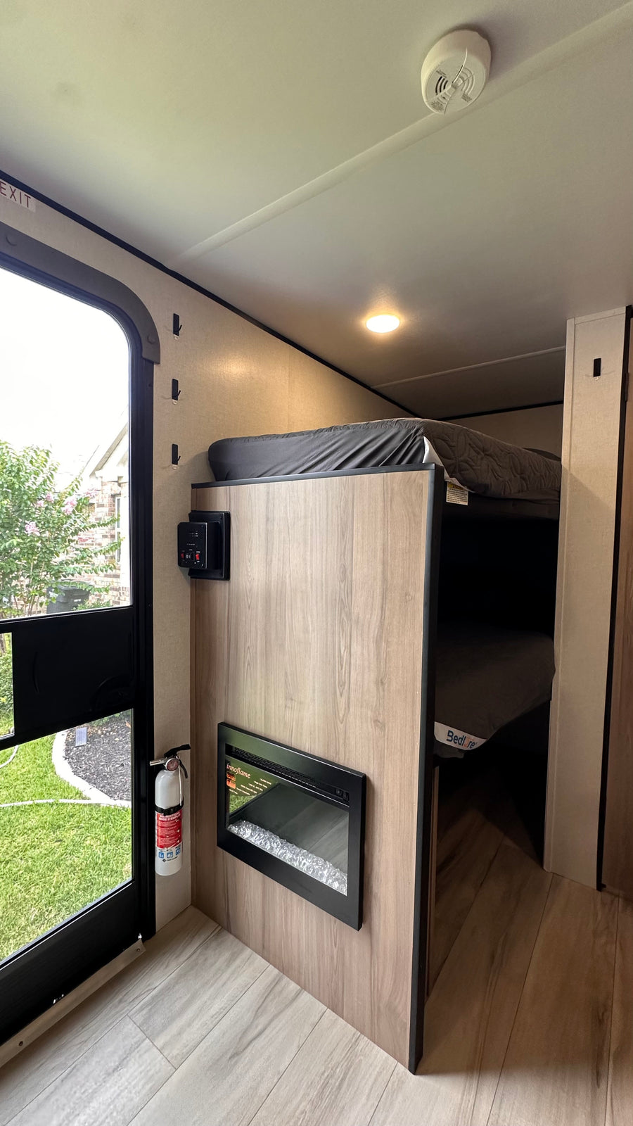 RV rental interior features bunk beds, a wall-mounted electric fireplace, and controls. Safety includes an extinguisher by the exit.