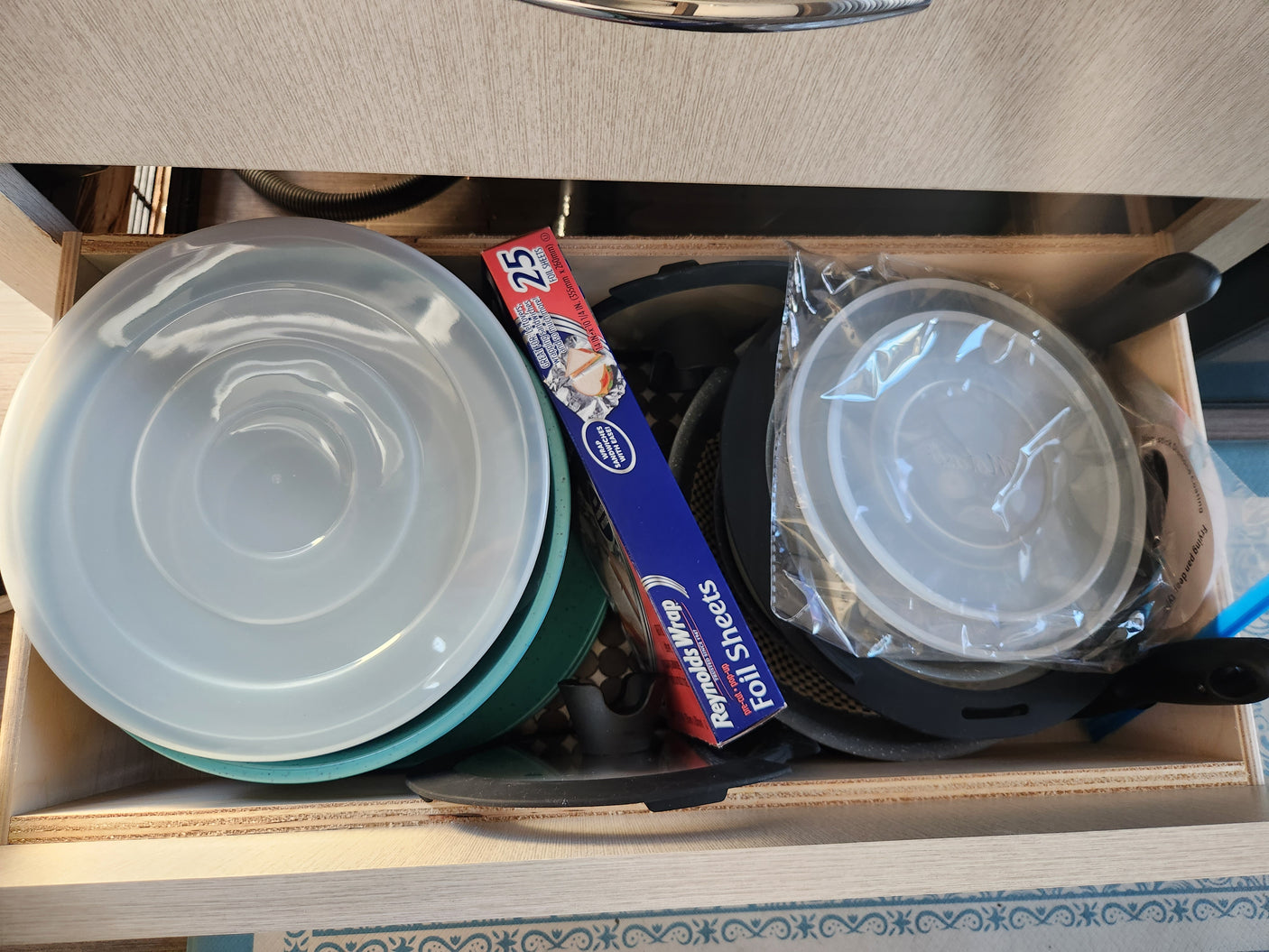 An RV rental kitchen drawer neatly holds cooking supplies like pans, plastic lids, and Reynolds Wrap foil sheets for convenient meal prep.