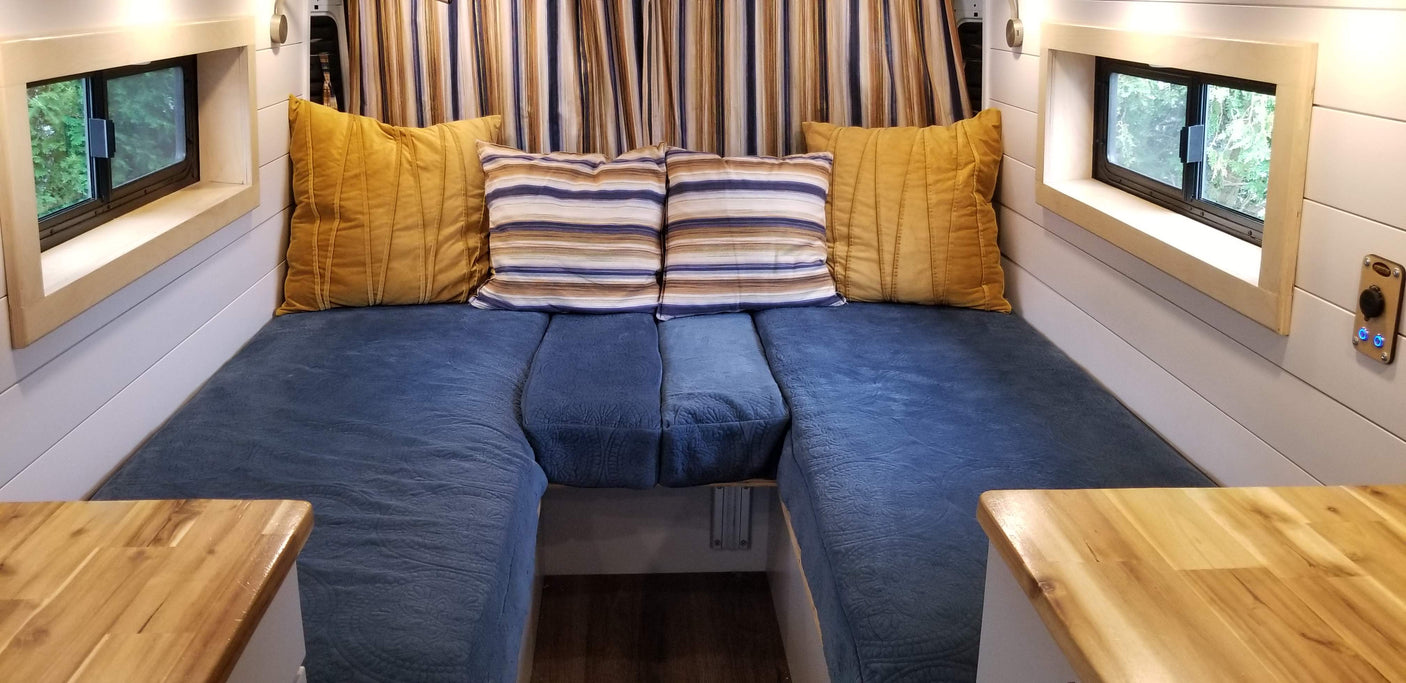 Cozy RV rental interior featuring blue U-shaped seating with colorful pillows, framed windows, and wooden countertops.