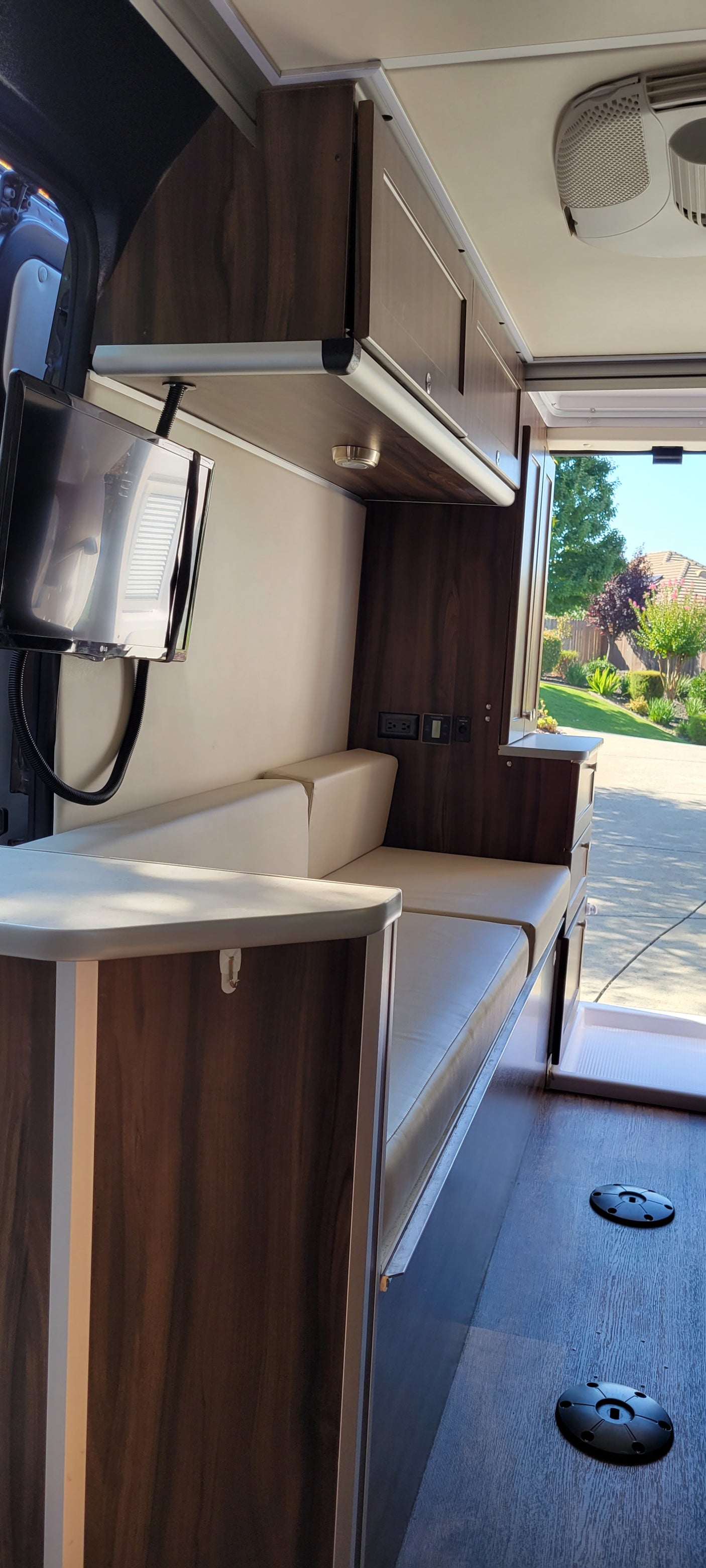 Modern RV rental interior with sleek dark wood cabinetry, light upholstered seating, a TV, and floor mounts, inviting the outdoors in.