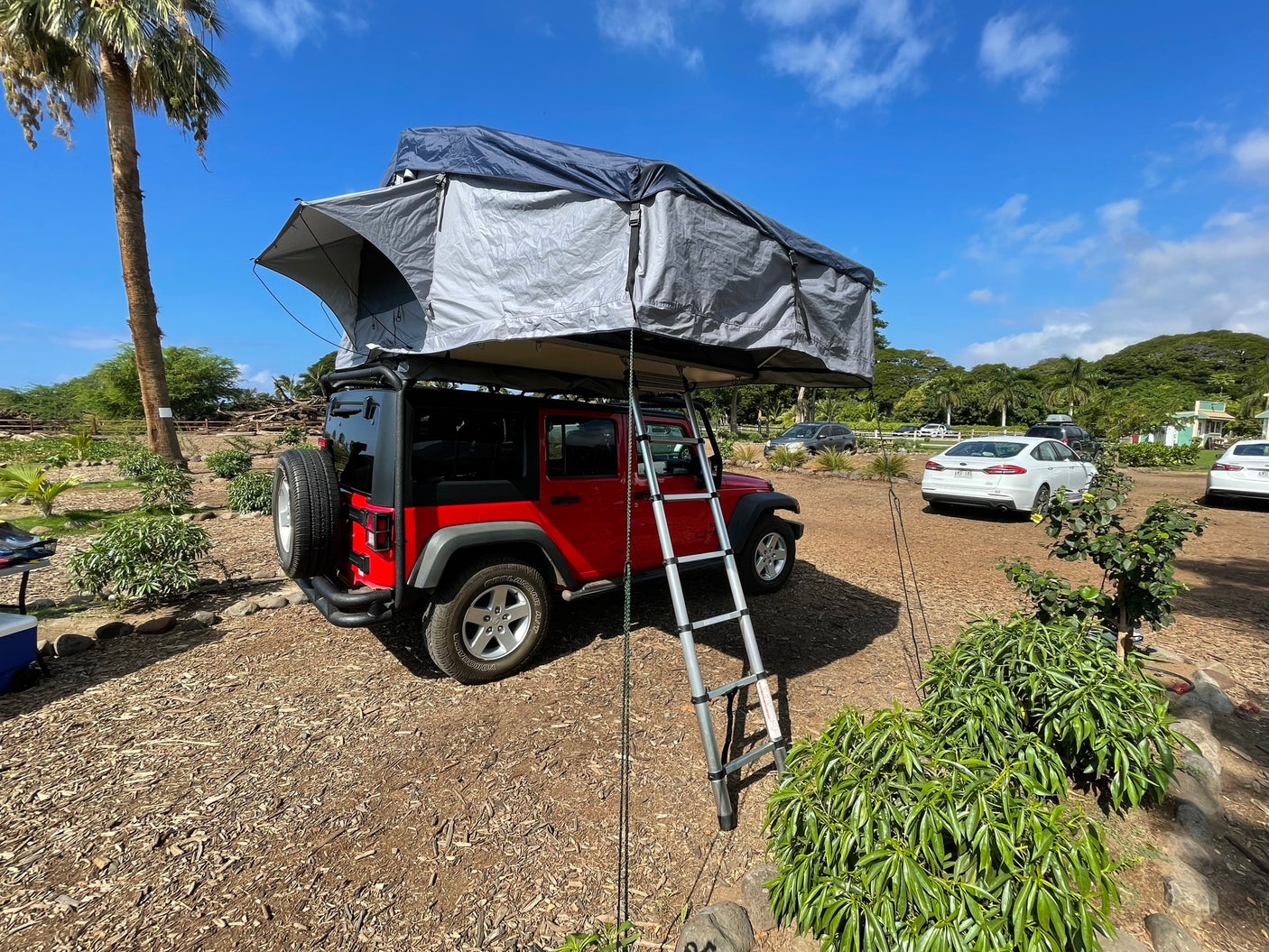 Red Jeep with deployed rooftop tent and ladder, a perfect RV rental for camping and outdoor adventures.