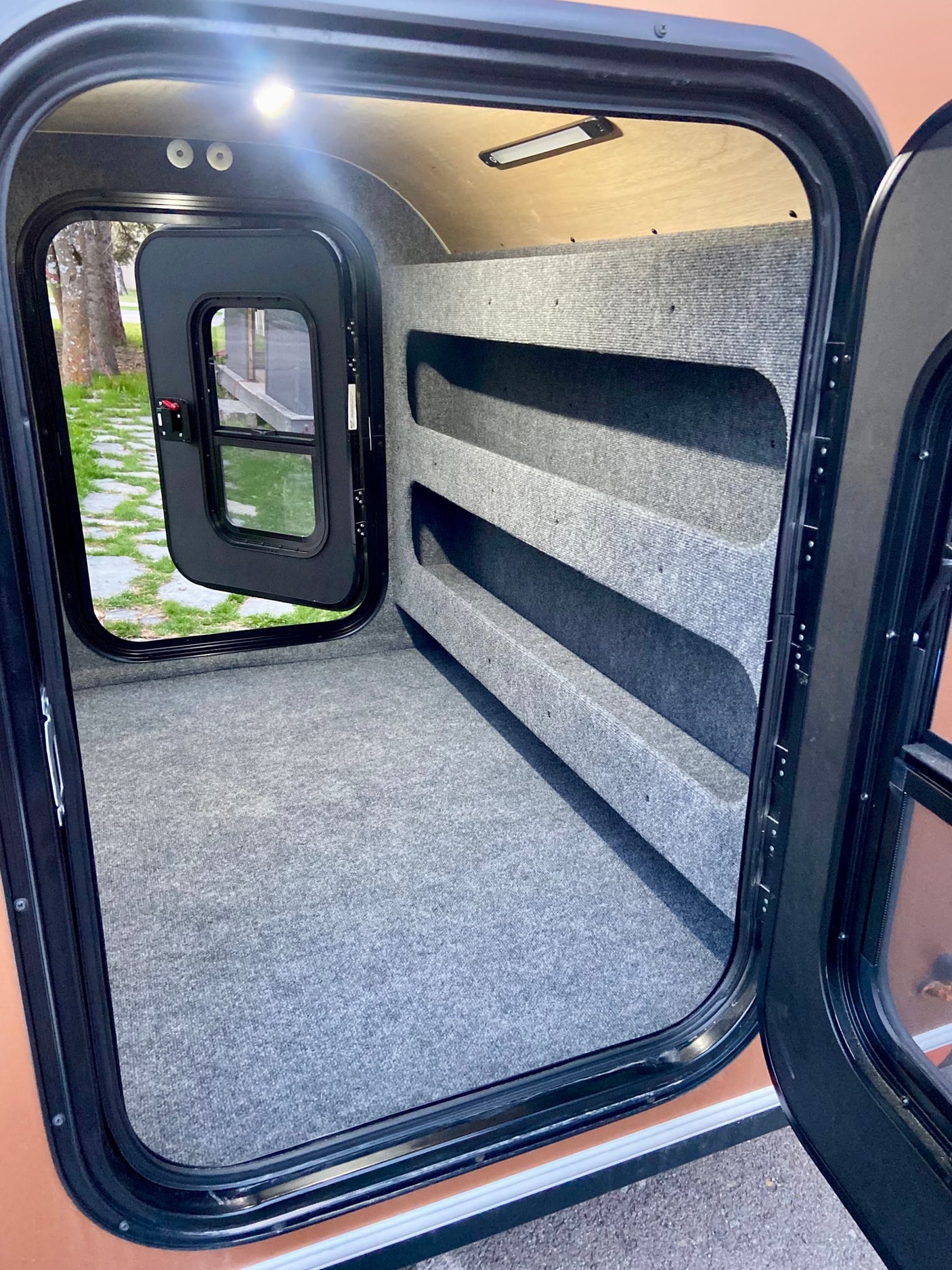 Explore this RV rental's cozy, carpeted interior, featuring integrated shelving for storage and ample space for sleeping.