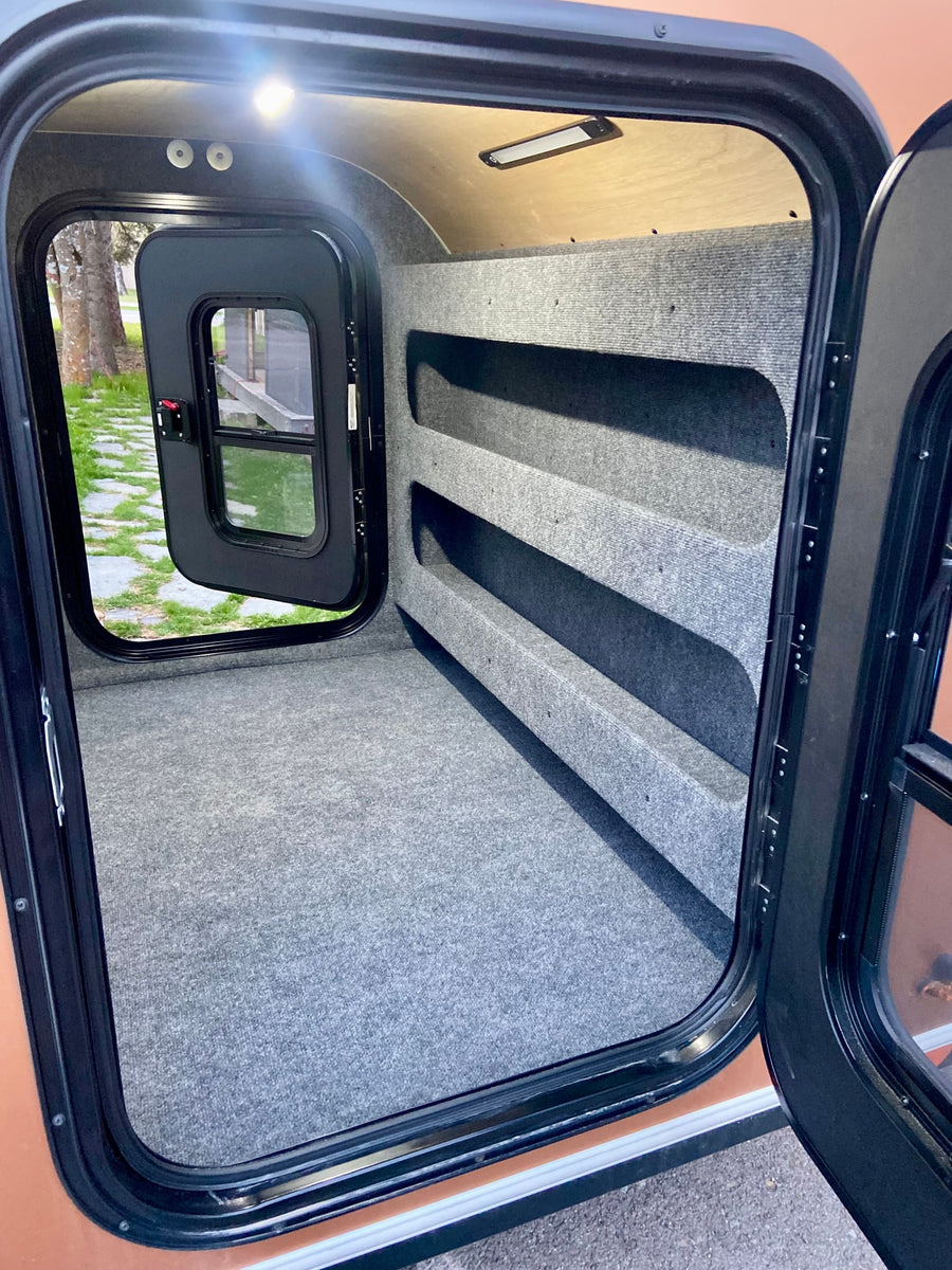 Explore this RV rental's cozy, carpeted interior, featuring integrated shelving for storage and ample space for sleeping.