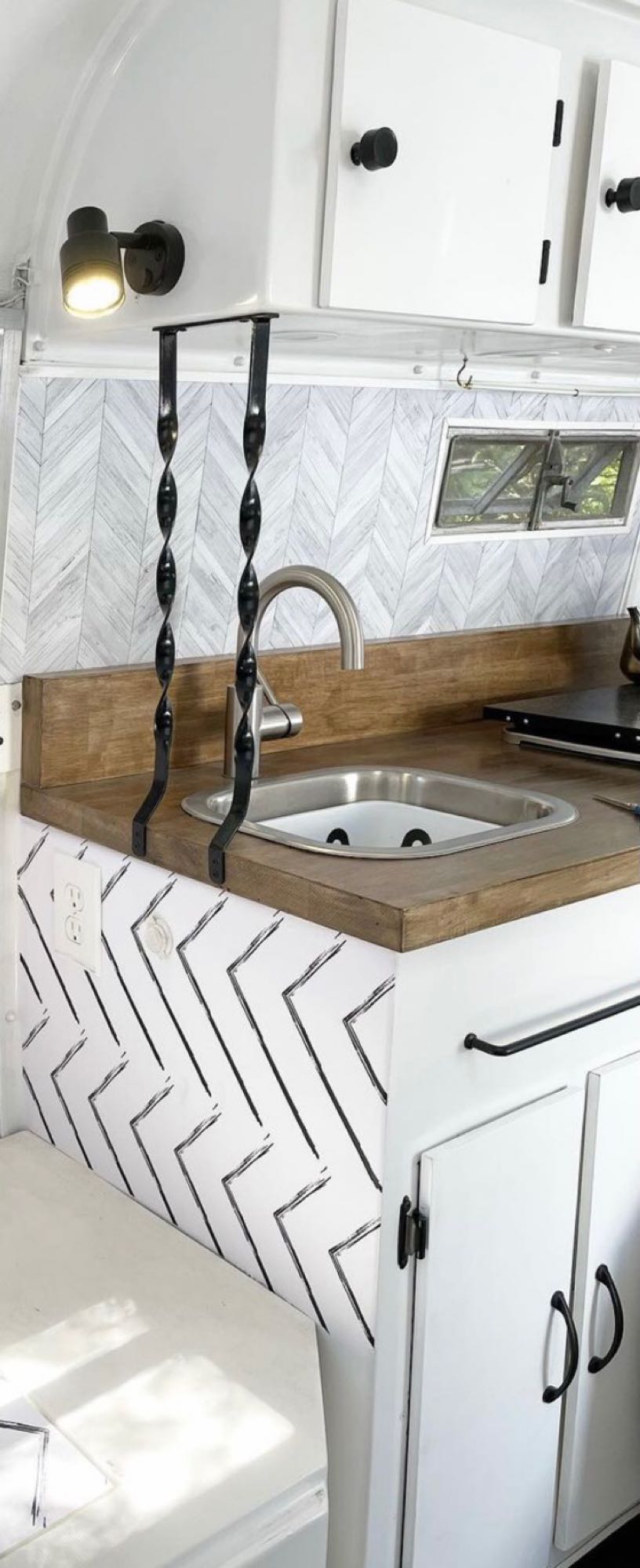 Modern RV rental kitchenette featuring a sleek sink, wood counters, and stylish chevron patterns. Compact & well-equipped.