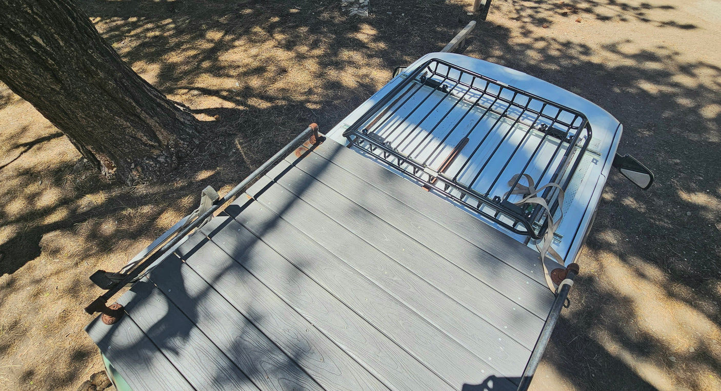 Overhead of an RV rental: custom roof deck, front cargo rack. Parked under dappled tree shade. Ideal for outdoor adventures.