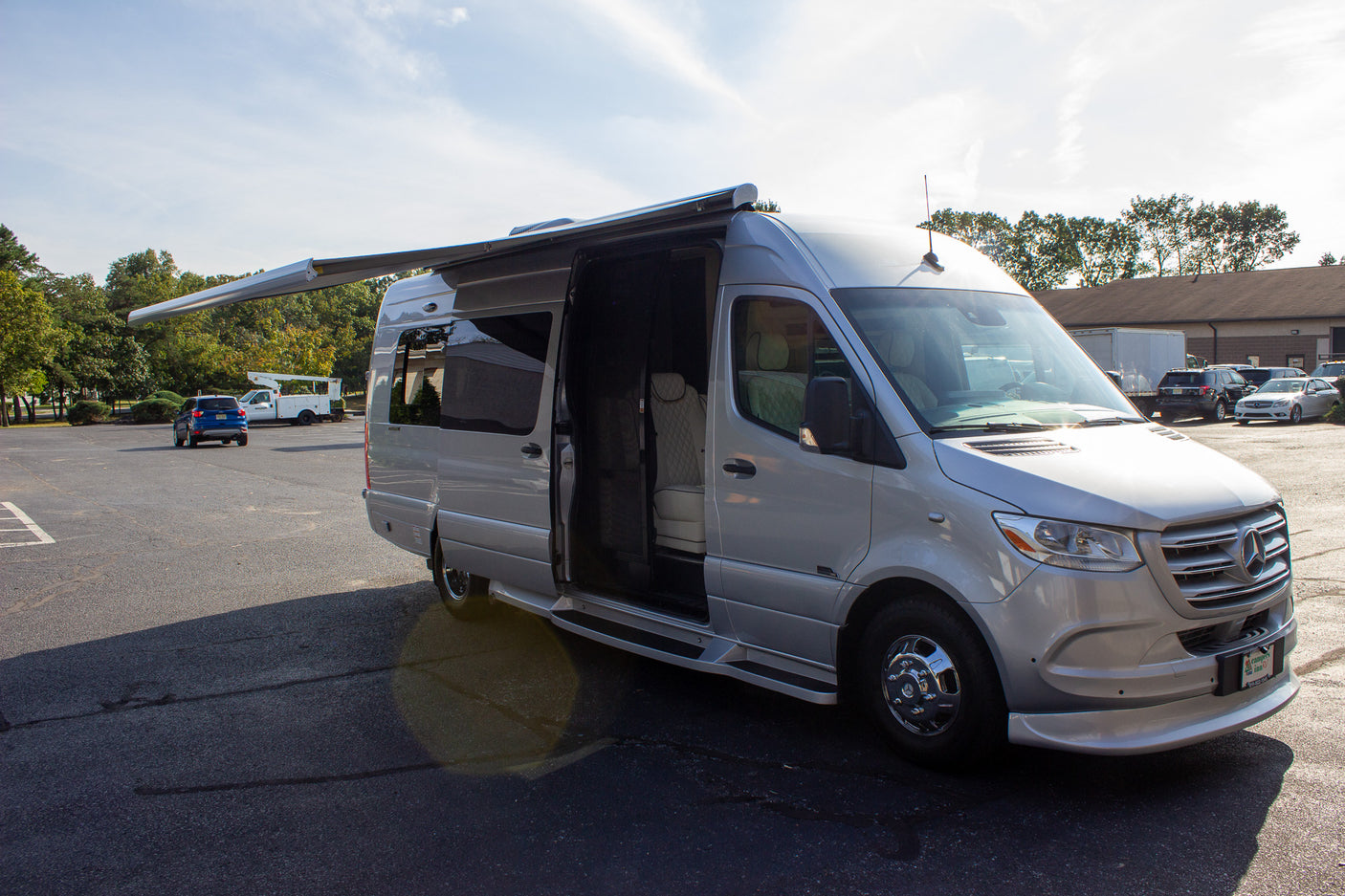 Silver Mercedes-Benz Sprinter luxury RV rental with extended awning, side door open, in a sunny lot.