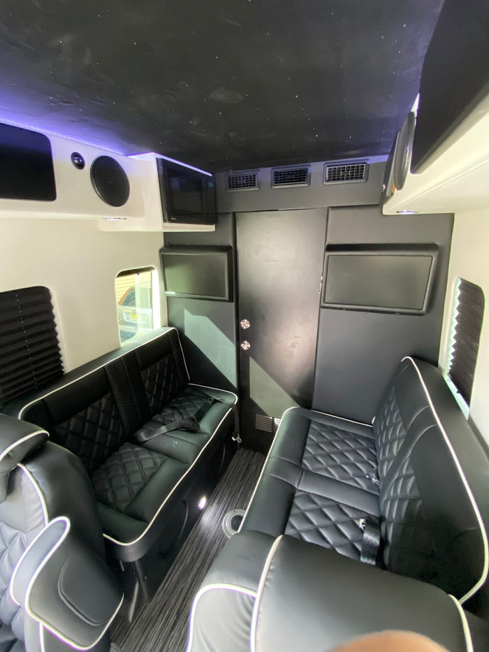 Inside a stylish RV rental: black quilted seating, multiple screens, microwave, and a unique starry ceiling design.
