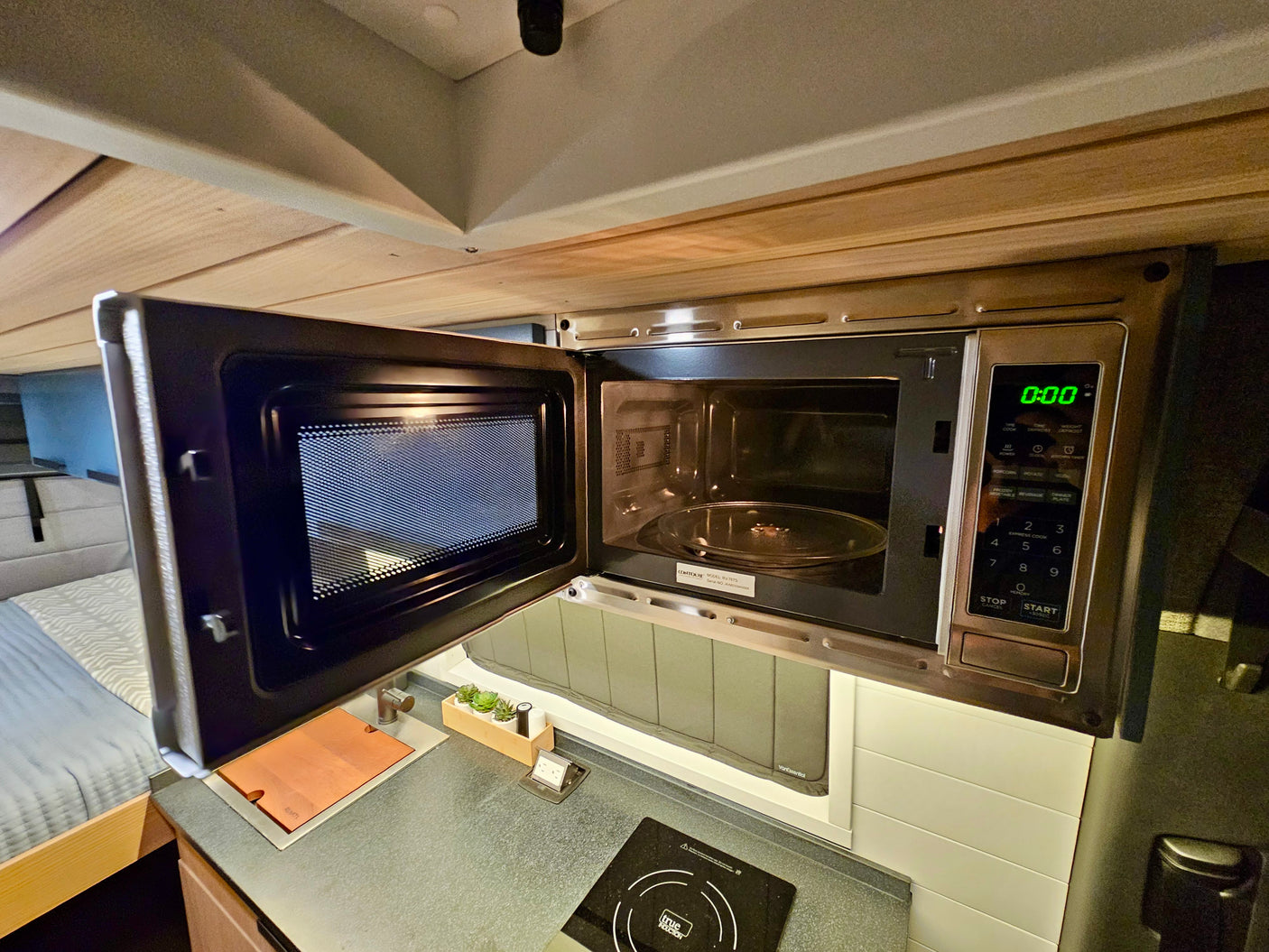 This RV rental features a modern, compact kitchen with an open microwave, induction cooktop, and a small sink.
