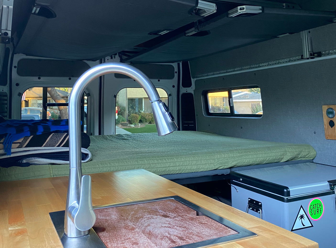 Cozy RV rental interior: compact kitchen with modern faucet & wood counter, a comfy bed, and fridge.