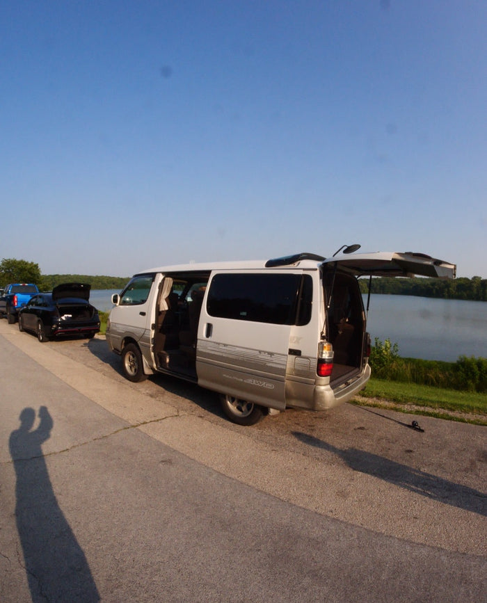 parked roadside by a scenic lake. Ideal for outdoor travel and leisure.|A white Toyota van