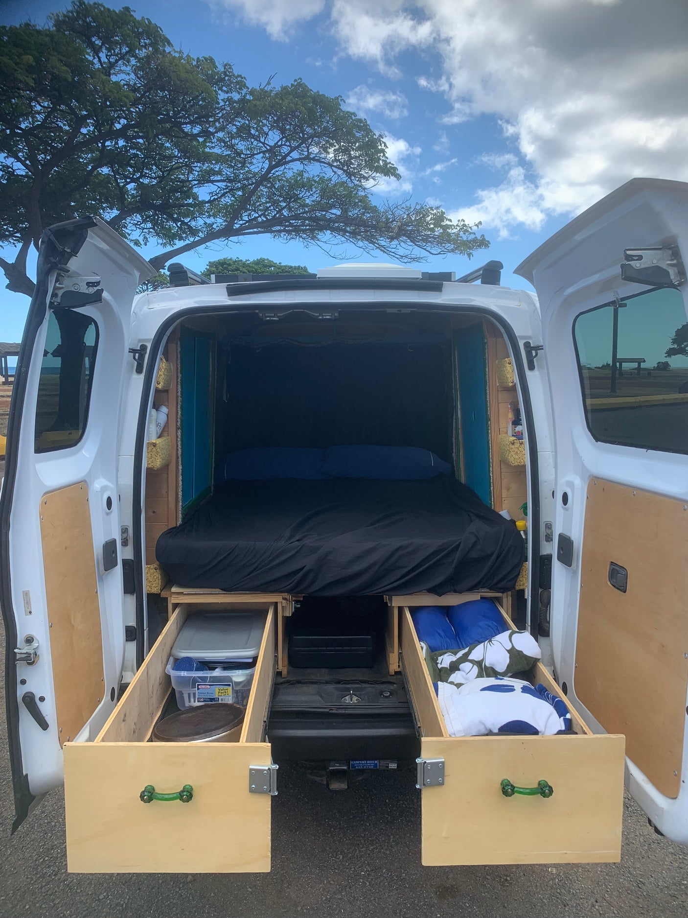 Inside an RV rental, this camper van interior features a cozy bed and custom wooden storage units with hinged panels.