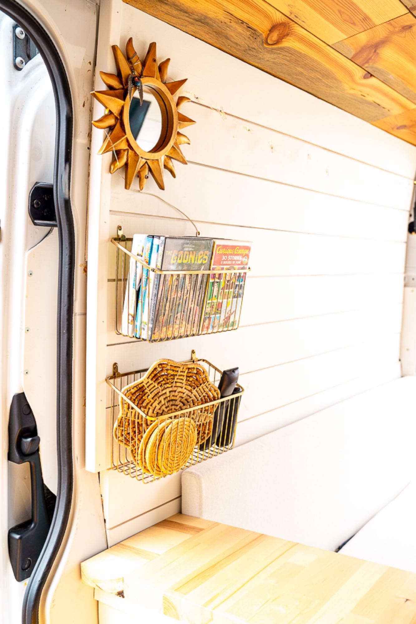 RV rental interior showcases clever storage: gold wall baskets with DVDs & coasters, and a decorative sun mirror.