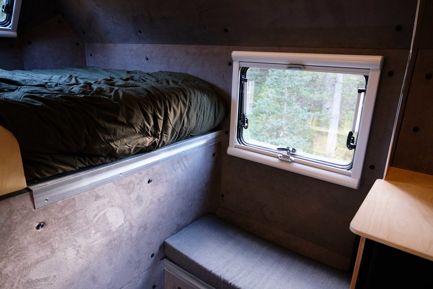 Explore this cozy RV rental interior featuring a comfortable bed, window with nature views, and a compact seating area.