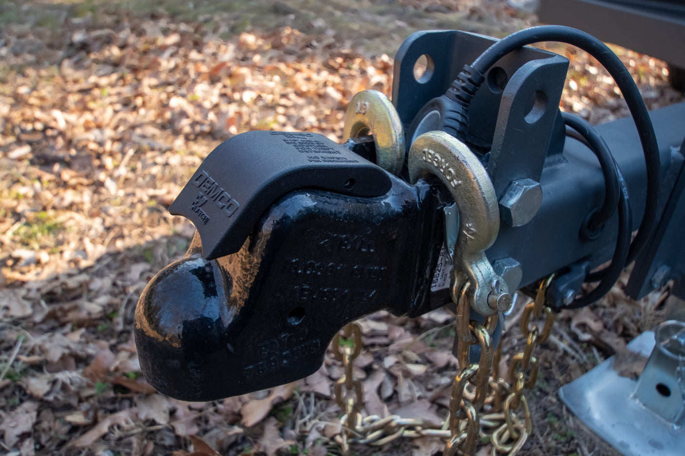 Close-up of a black trailer hitch coupler with safety chains, essential for safe RV rental towing. Features a DEMCO EZ-LATCH.