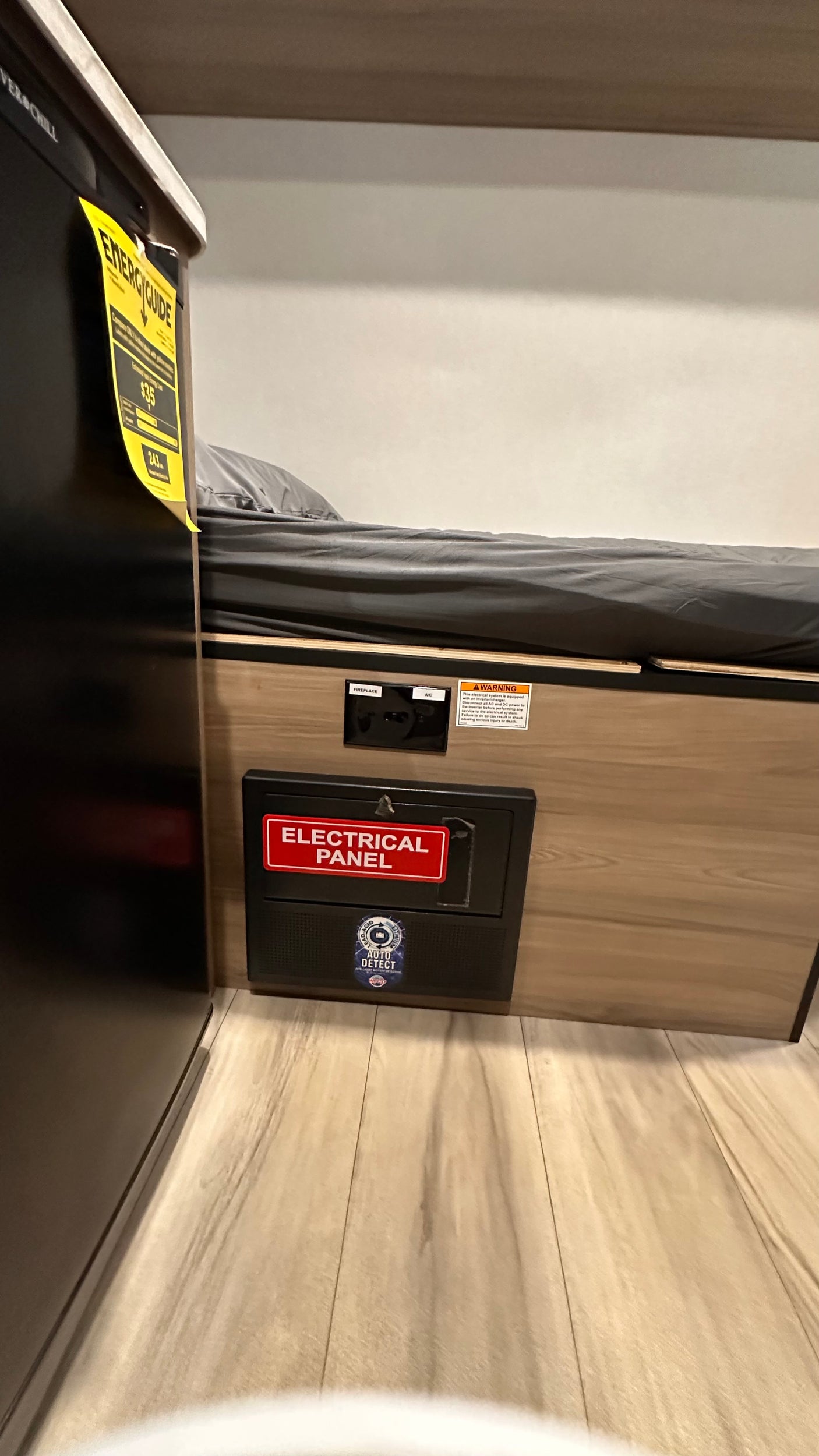 RV rental interior featuring a compact bed, an accessible electrical panel, and a refrigerator with an energy guide label.