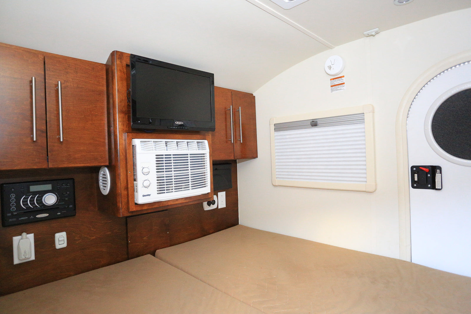 Inside an RV rental, a cozy bed, wood cabinets, TV, AC unit, and control panel provide comfortable amenities.