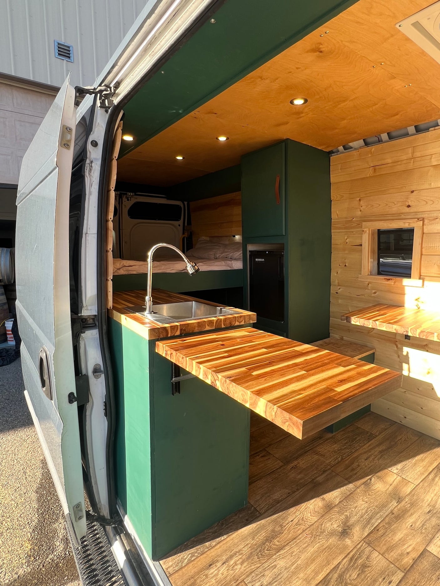 Custom RV rental interior with green cabinetry, wood paneling, and a unique pull-out table, perfect for van life.
