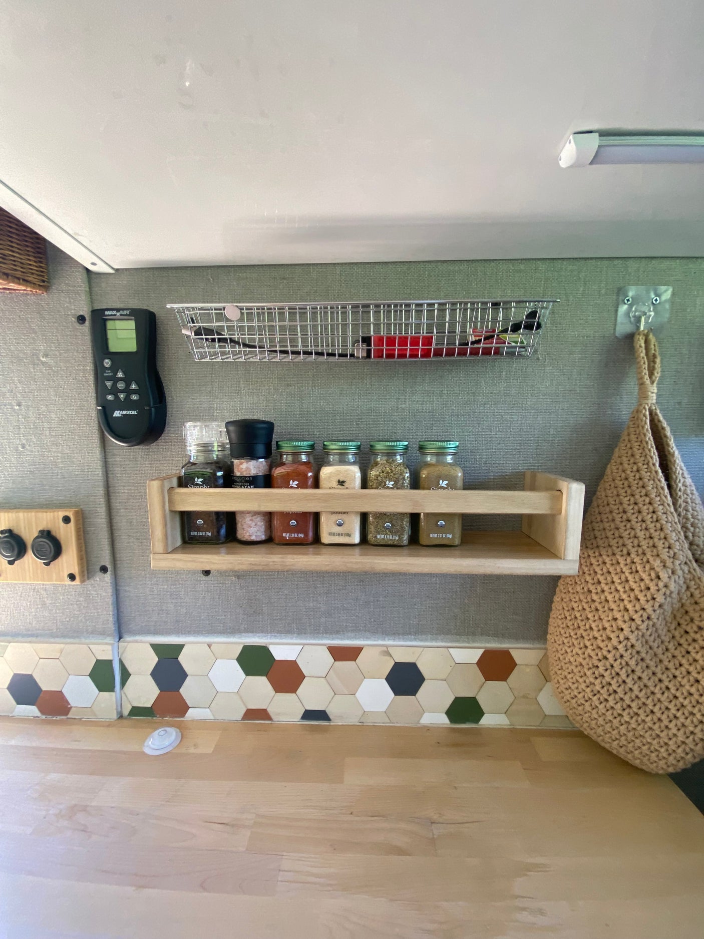 This RV rental kitchen features a spice rack, hexagonal backsplash, wooden counter, and a Maxxair fan control.