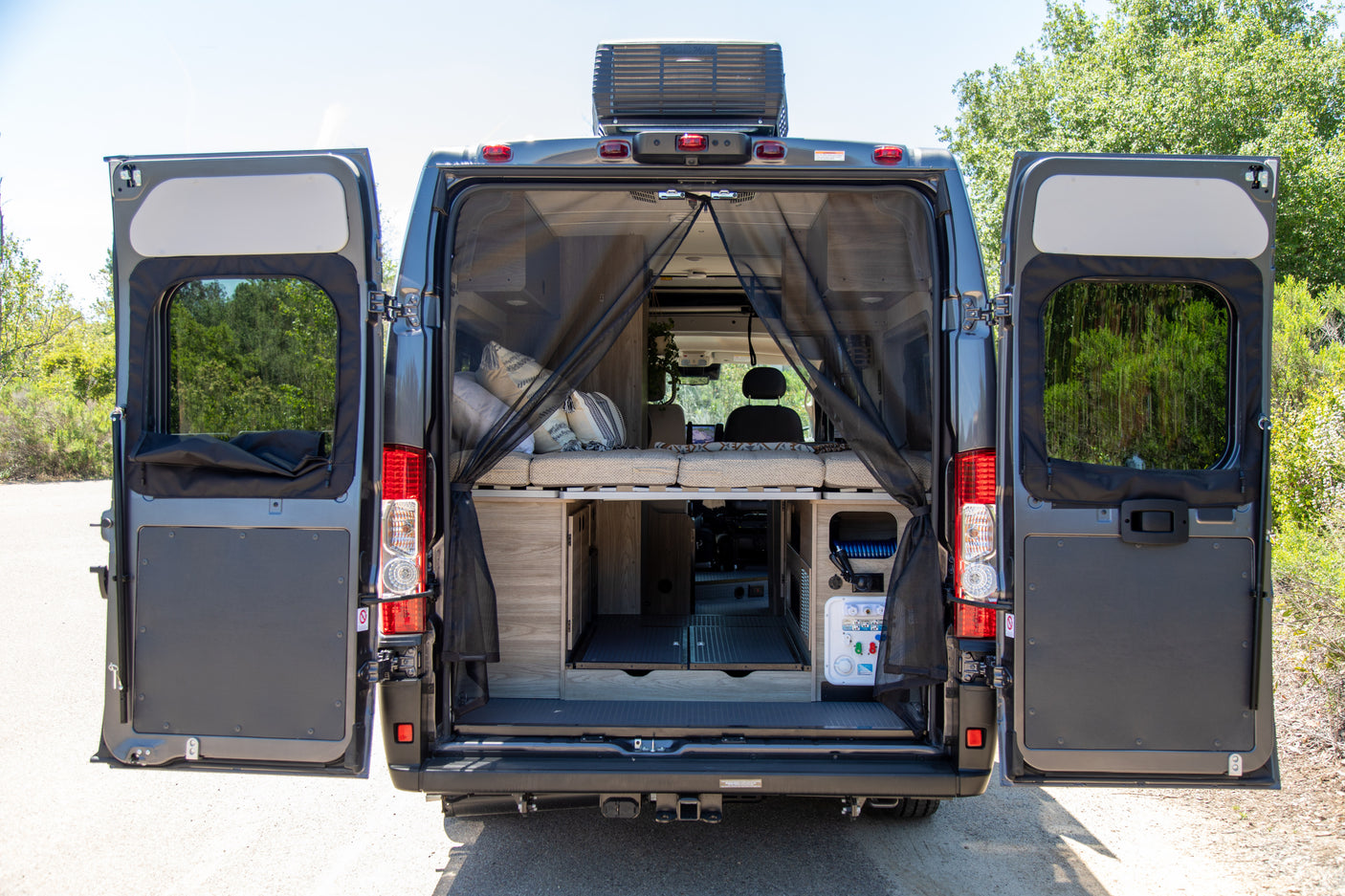 Open back doors of an RV rental reveal a custom interior with a bed, storage, and mosquito screen for outdoor adventures.