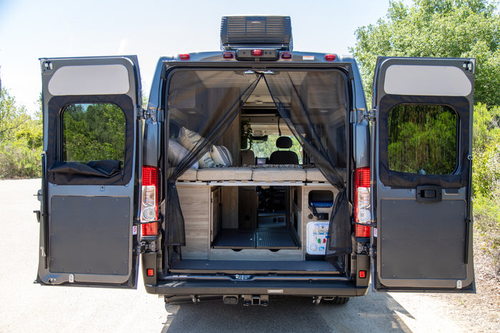 Open back doors of an RV rental reveal a custom interior with a bed, storage, and mosquito screen for outdoor adventures.