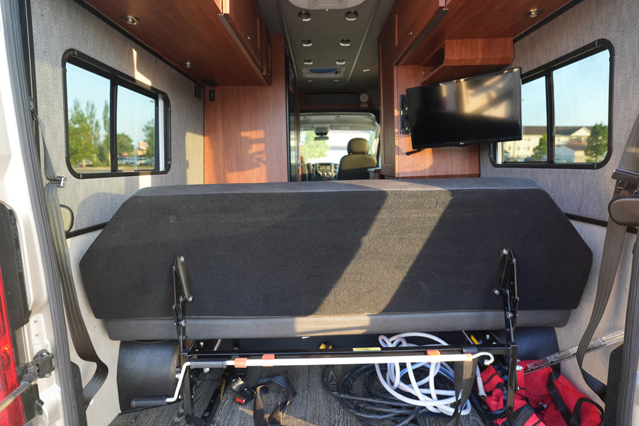 Bright RV rental interior with a convertible rear bed, under-seat storage, side windows, and a mounted TV.