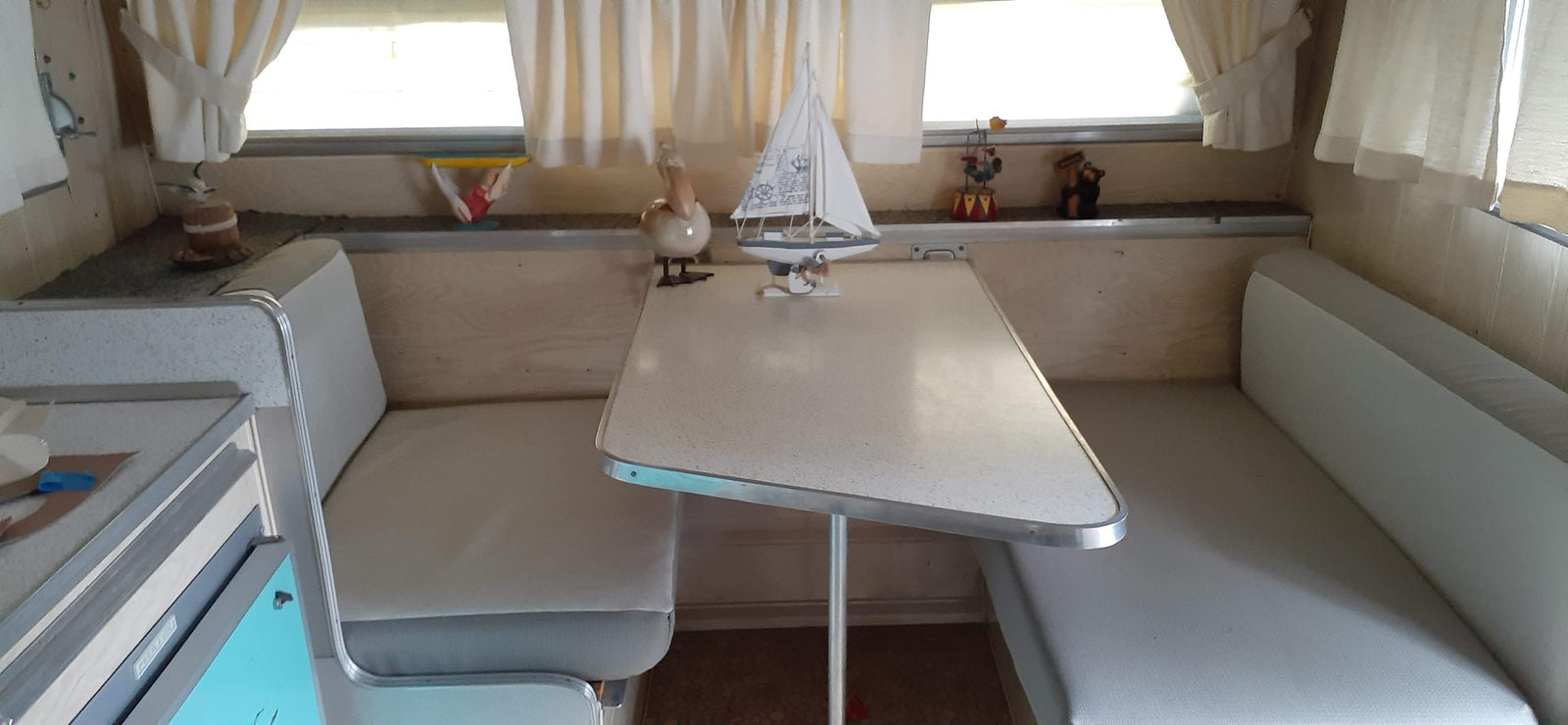 A vintage RV rental interior: a dining booth with light cushions, center table, and eclectic decor on the shelf.
