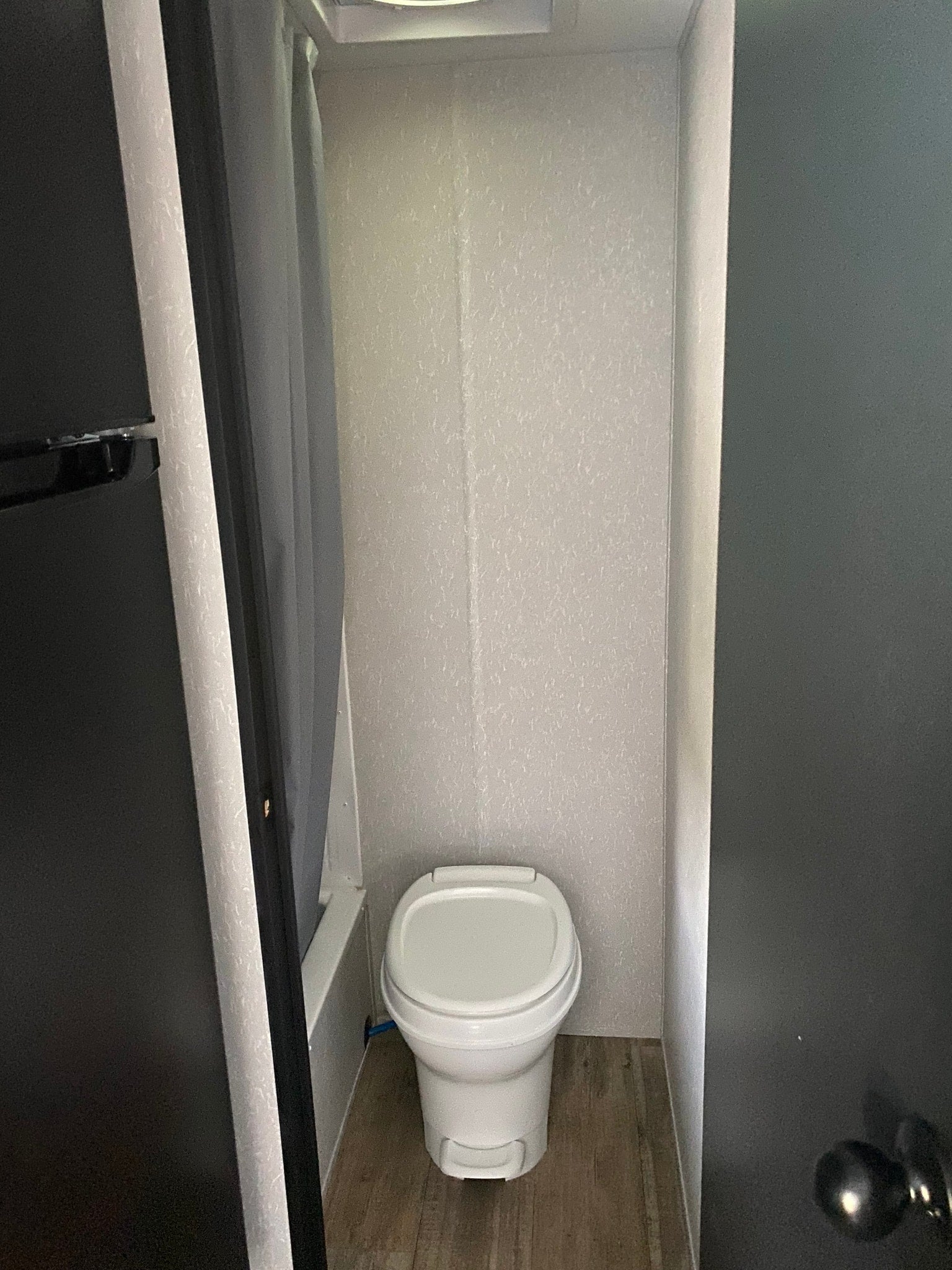 An RV rental's compact bathroom, featuring a white toilet, light walls, and wood-look floor.