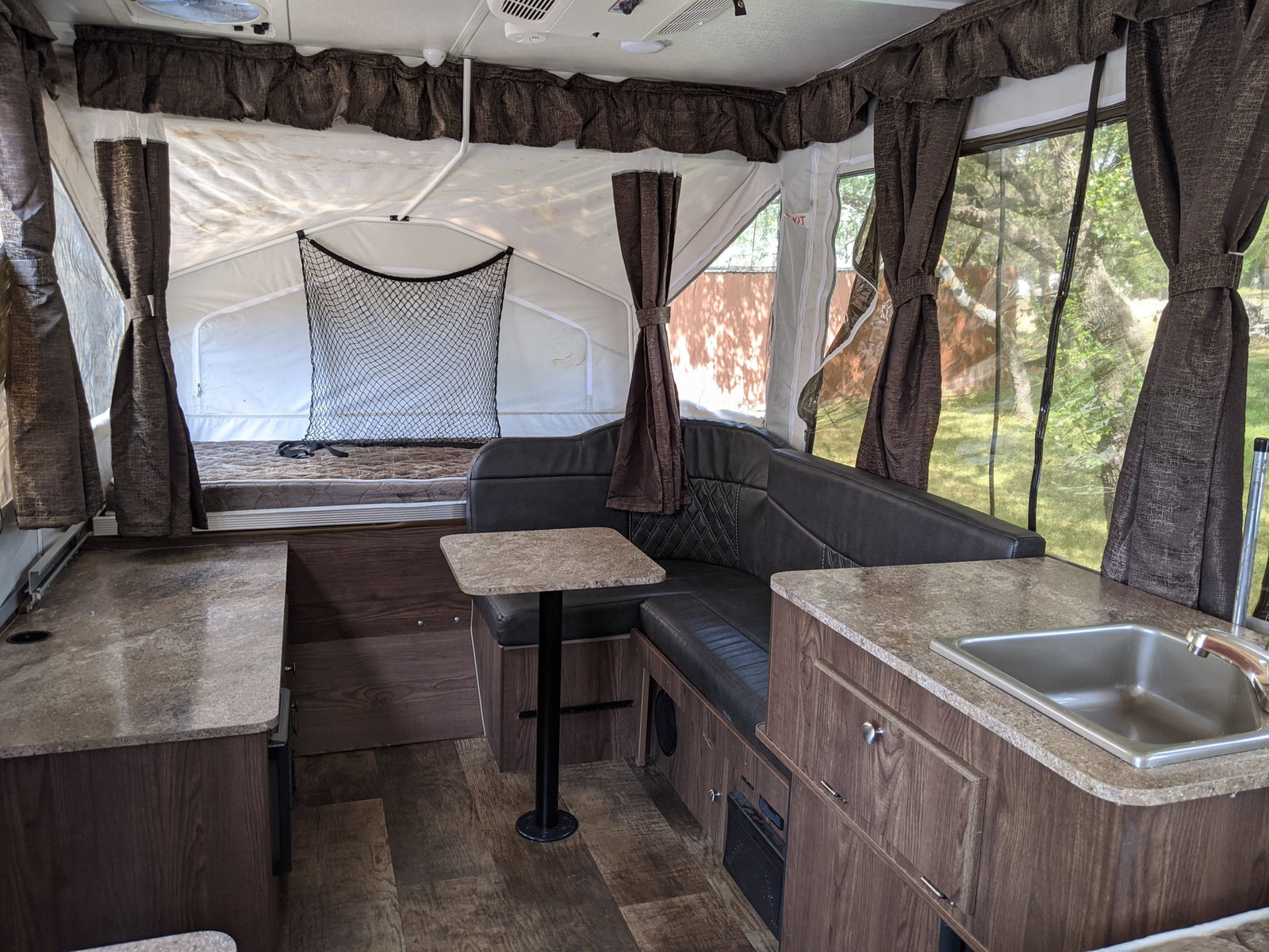 Spacious pop-up RV rental interior featuring a dinette, kitchen with sink, and sleeping area with privacy curtains.