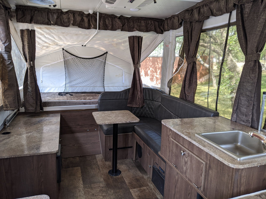 Spacious pop-up RV rental interior featuring a dinette, kitchen with sink, and sleeping area with privacy curtains.