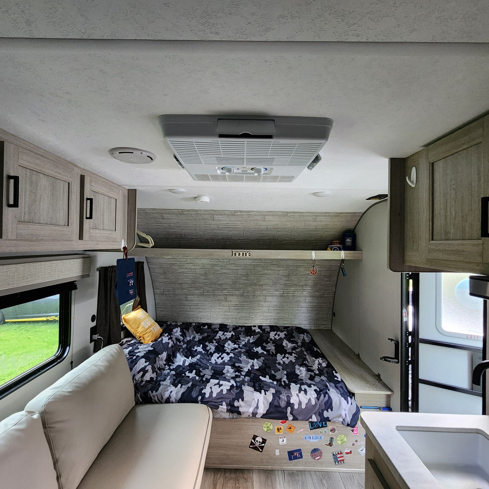 This RV rental interior offers a bed with camo bedding, a comfy sofa, and a small kitchen area, ideal for journeys.