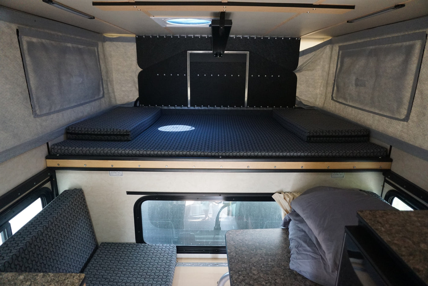 RV rental interior: A bed/lounge area with patterned gray cushions and a dining table on the right. — photo 8