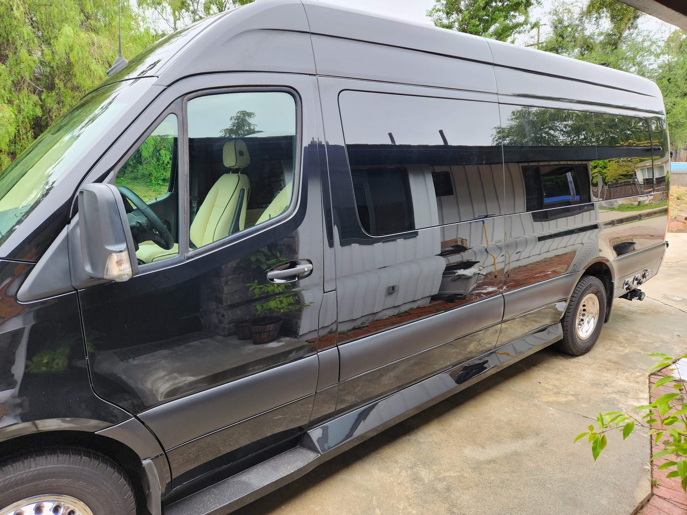 Side view of a glossy black luxury Sprinter van, ideal for rv rental. Parked on concrete with tinted windows and cream seats.
