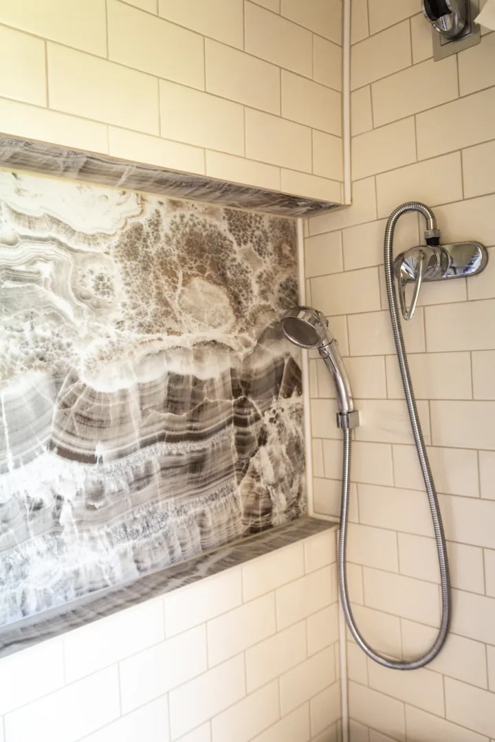 RV rental shower with sleek off-white subway tiles, a unique veined stone niche, and a modern handheld showerhead.