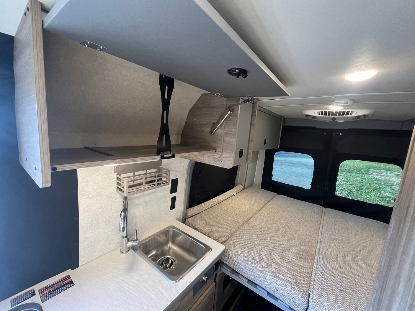 RV rental interior: cozy campervan kitchenette with sink, open overhead storage, and comfortable bed for your next adventure.