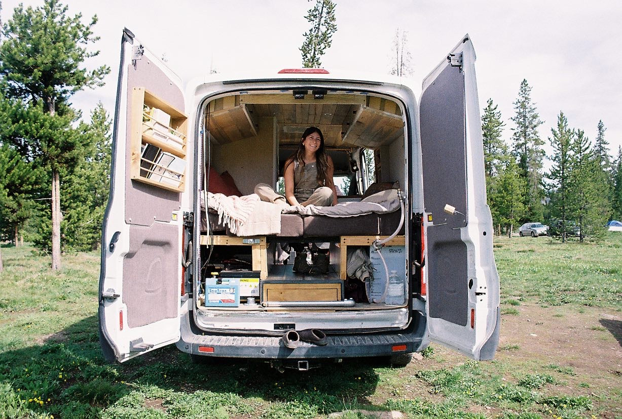 Smiling woman in her custom camper van, set up for adventure. An ideal RV rental for exploring nature and van life travel.