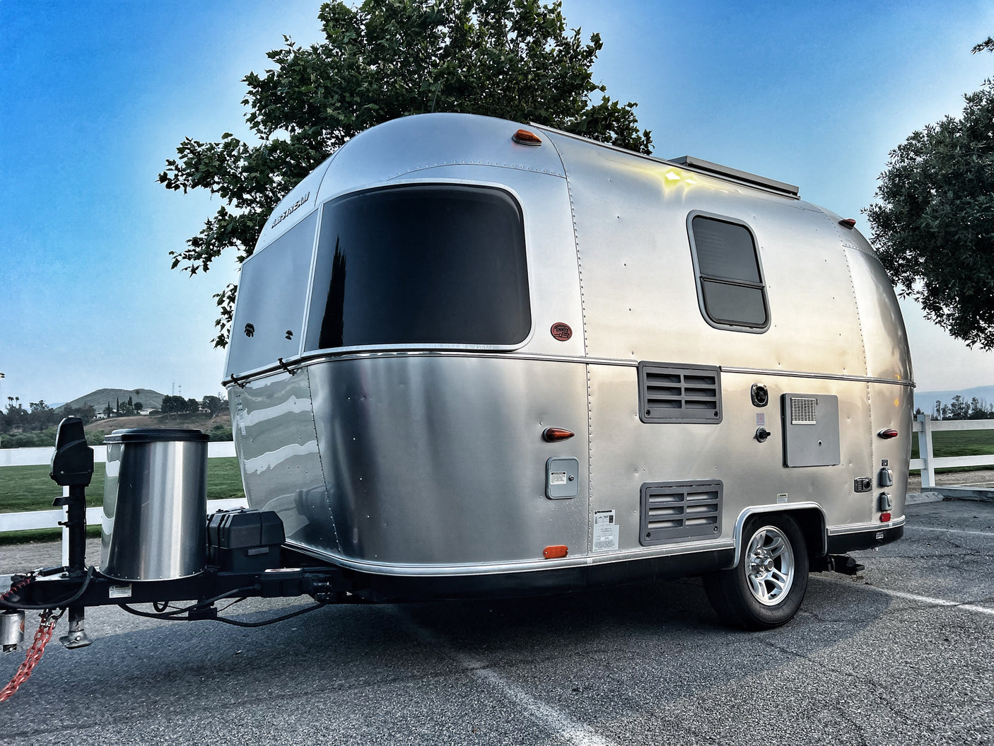 Sleek silver Airstream travel trailer, hitched up for an RV rental adventure. Parked on asphalt under a clear blue sky.